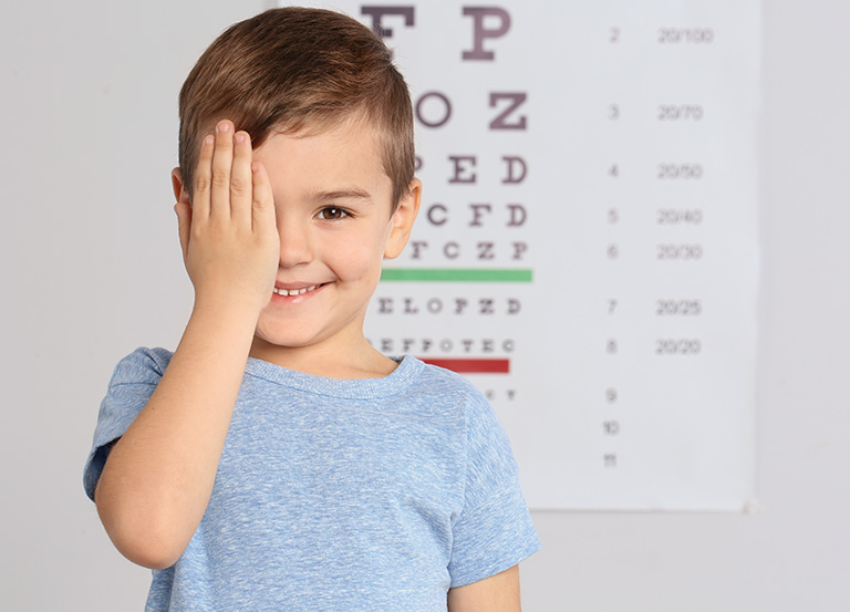 Uśmiechnięty chłopiec zasłania jedno oko podczas badania wzroku