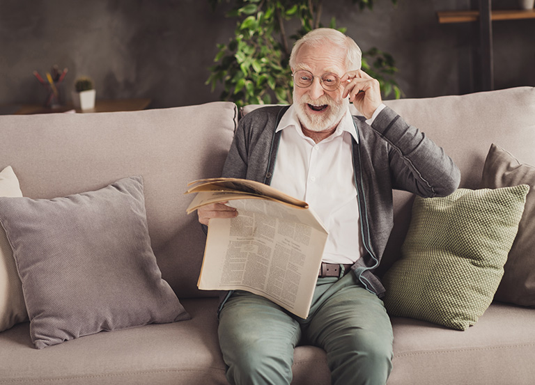 Szczęśliwy starszy mężczyzna w okularach czyta gazetę